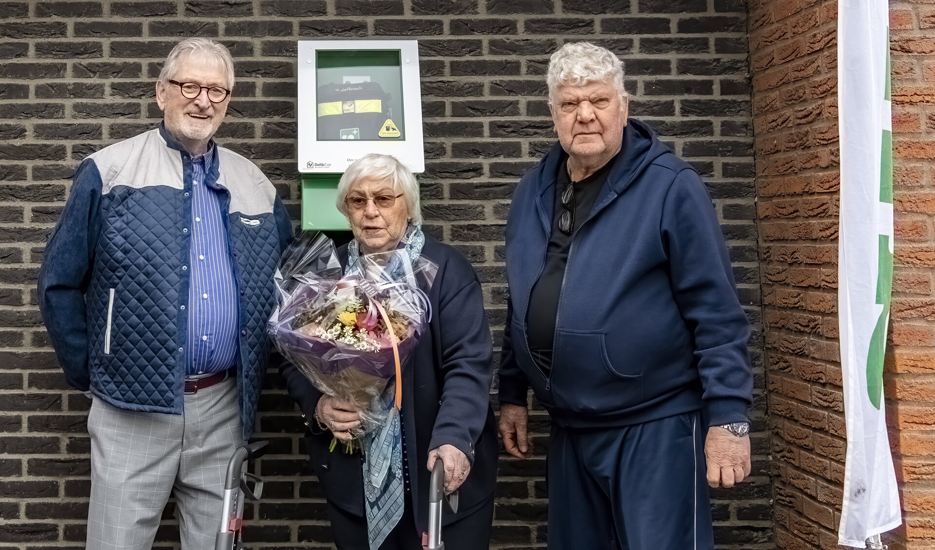 De oudste bewoonster Sonja van der Zee, hier geflankeerd door Maarten Kuiper (links) en Hans Reijgwart, onthulde de AED.