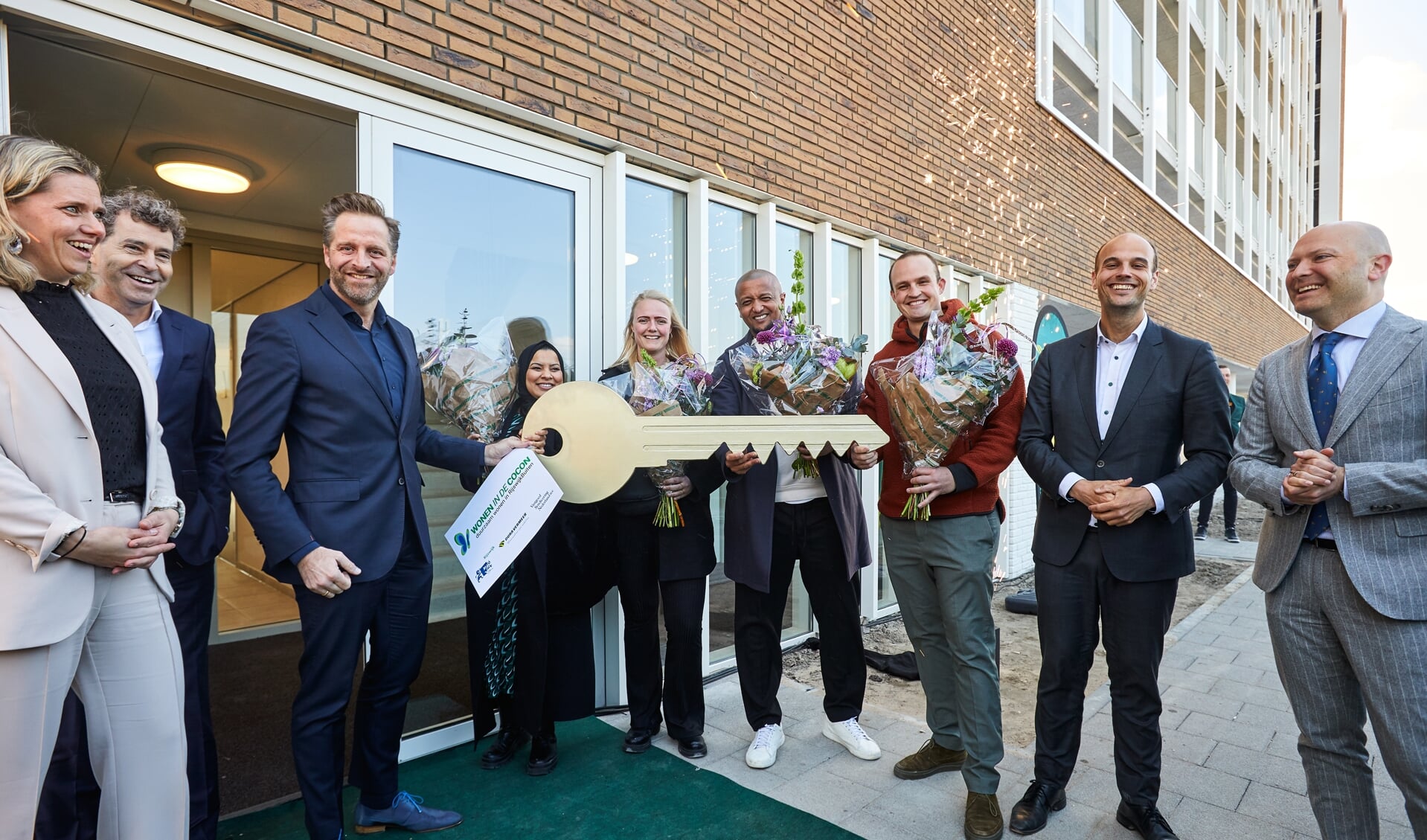 Minister Hugo de Jonge (links) overhandigt symbolisch een enorme, ‘gouden’ sleutel aan vier van de gelukkige nieuwe huurders. Rechts: wethouder Gijs van Malsen. 