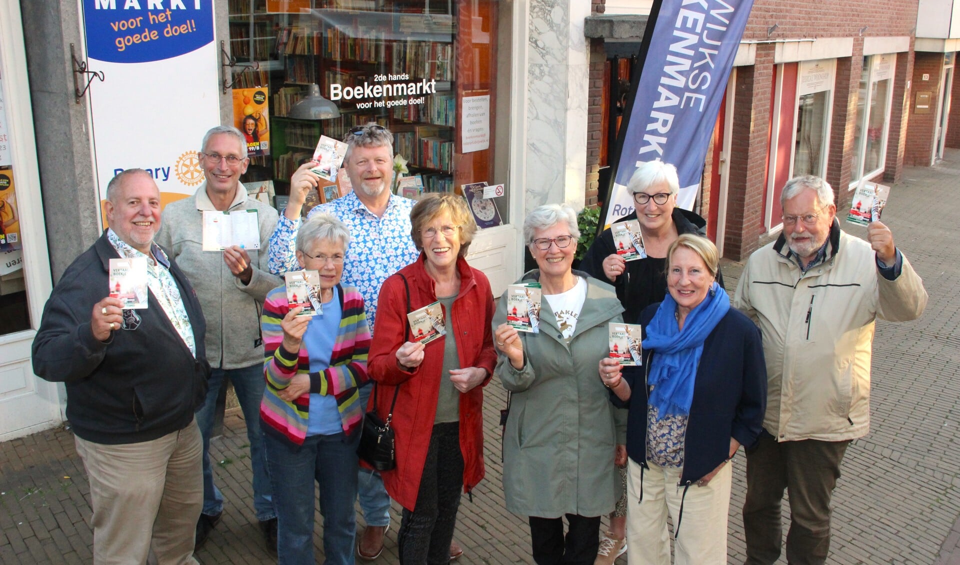 Liesbeth Kromhout (met rode jas) wordt omringd door Rijswijkers die hebben geholpen bij de productie van het vertaalboekje. Op de achtergrond het boekwinketje van de Rijswijkse Rotary Club.