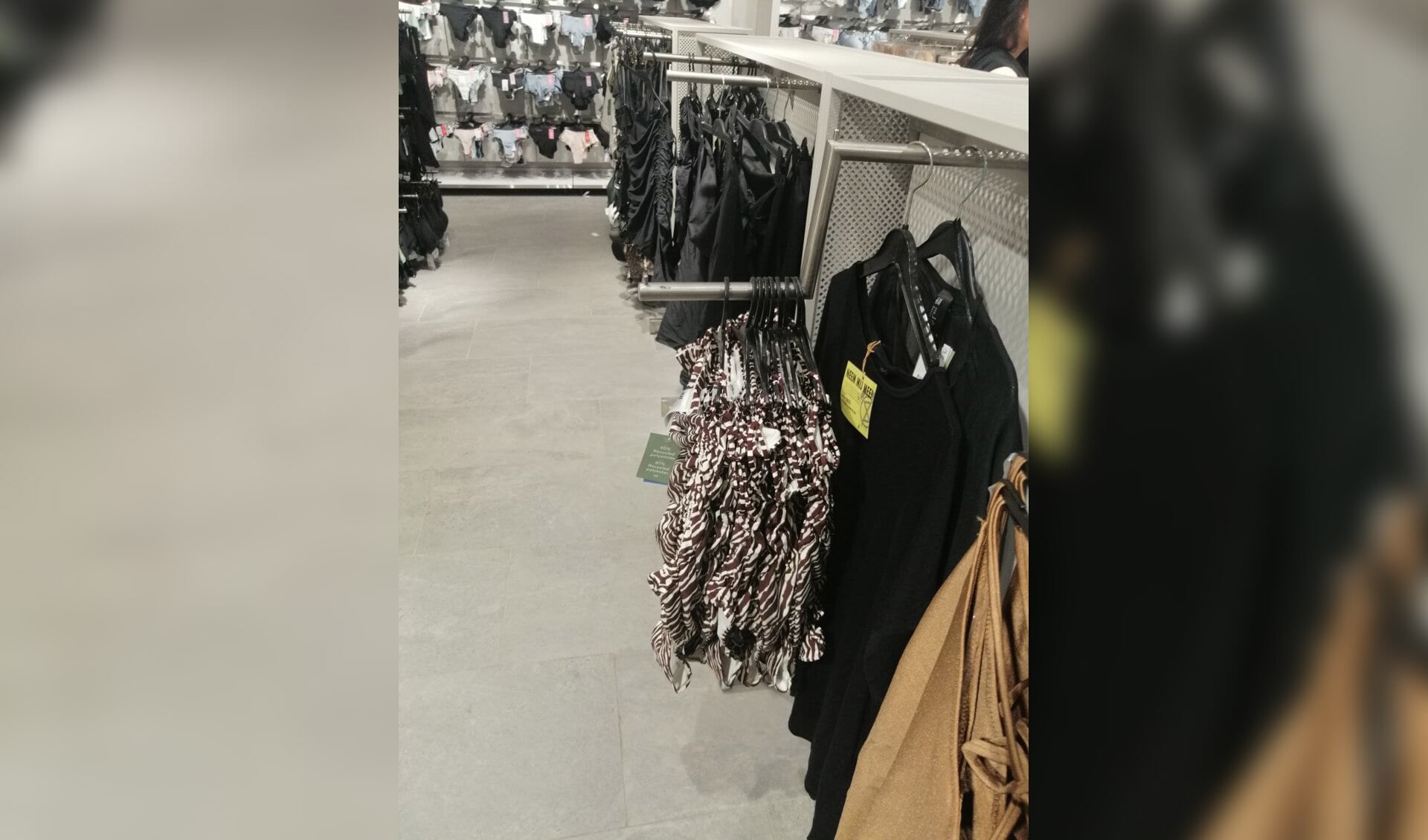 De tweedehands kleding werd tussen de kleding van de winkel gehangen.
