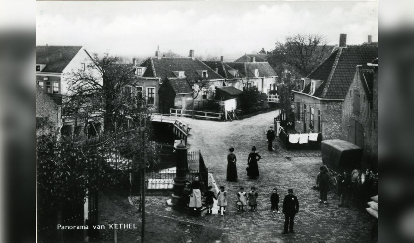 Het centrum van het dorp Kethel omstreeks 1905, gezien vanuit een woning op de hoek van de Dorpsstraat, Noordeinde en Schiedamseweg, in de richting van de Kerklaan, de weg naar links bij het witte hek. Op de voorgrond staan kinderen bij de ‘Verspeekpomp’. Rechts de paardenstal van de Vergulde Valk.