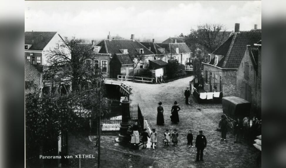 Het centrum van het dorp Kethel omstreeks 1905, gezien vanuit een woning op de hoek van de Dorpsstraat, Noordeinde en Schiedamseweg, in de richting van de Kerklaan, de weg naar links bij het witte hek. Op de voorgrond staan kinderen bij de ‘Verspeekpomp’. Rechts de paardenstal van de Vergulde Valk.