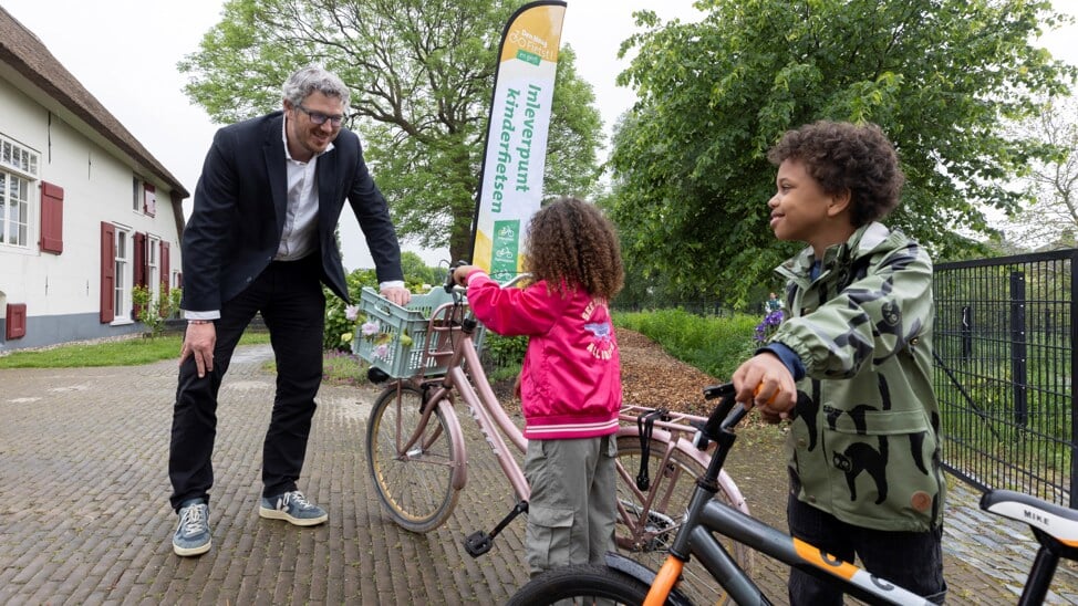 Wethouder Arjen Kapteijns neemt op stadsboerderij Op den Dijk een kinderfiets in ontvangst.