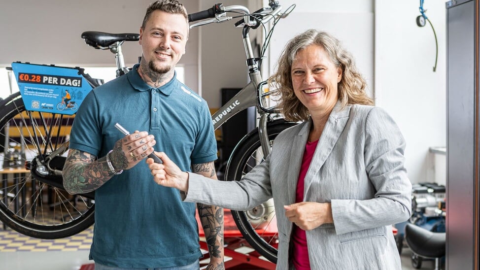 Thelma Petersen overhandigt symbolisch een dopsleutel aan werkplaats coördinator Glenn Rietveld bij de opening van de sociale fietswerkplaats van Biesieklette.