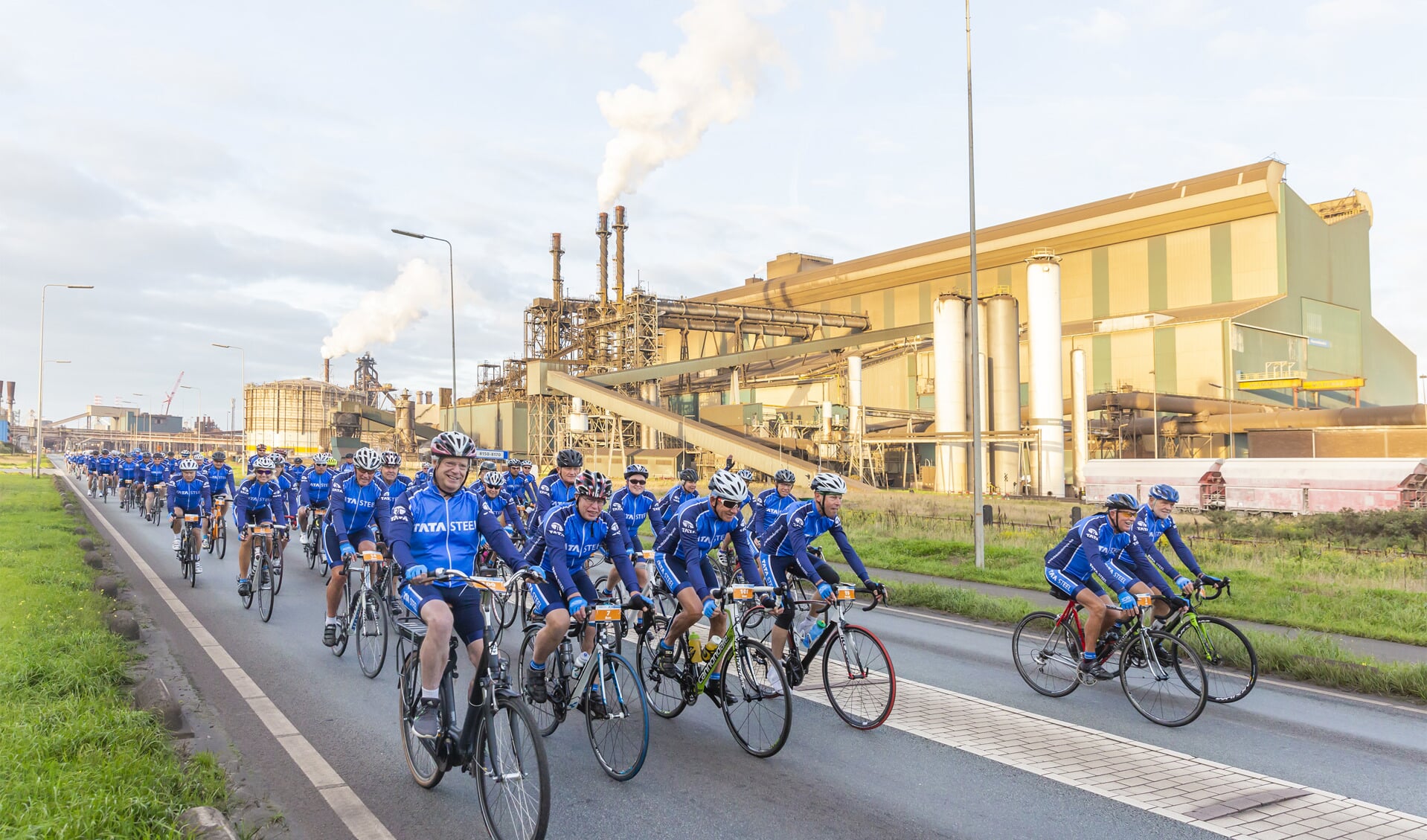 De wielrenners bij het passeren van de staalfabriek, met linksvoor Hans Fischer, CEO van Tata Steel in Europa. (Foto: Tata Steel)