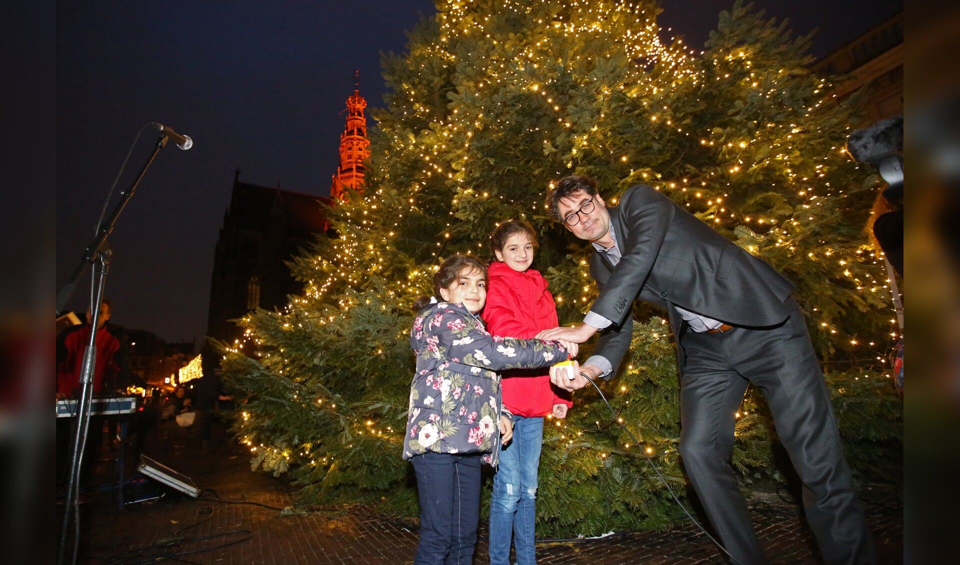 Wethouder Merijn Snoek poseert met de zusjes voor de gigantische kerstboom op de Grote Markt. (Foto: Rowin van Diest)