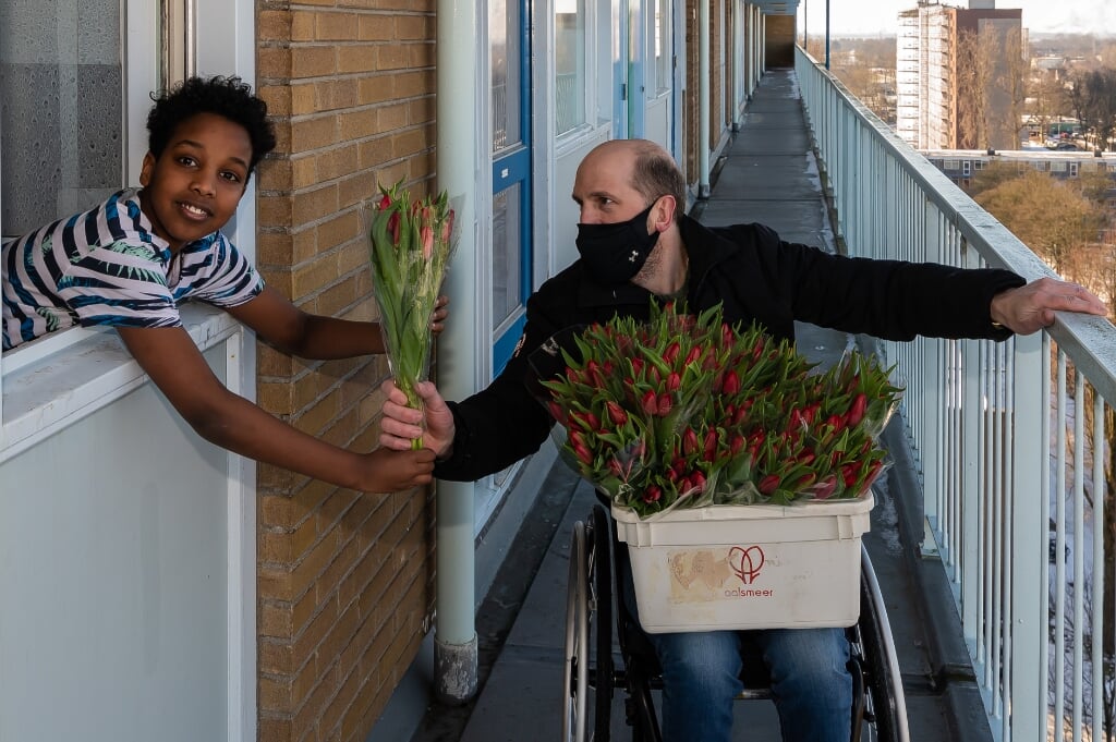Marwan krijgt via het raam een bosje tulpen van Melvin Smid aangeboden. 