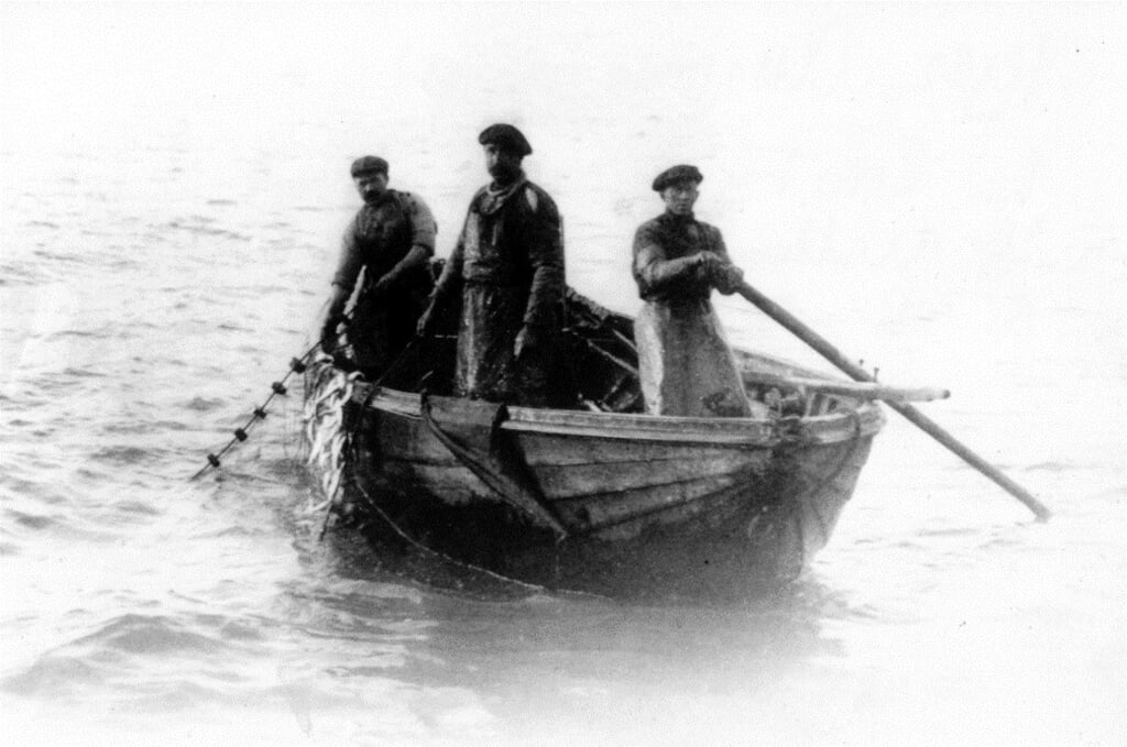 Foto uit 1932 van de vissers Cees Fijma, Willem Visser en K. de Graaf tijdens de ansjovisvisserij. De staande netten met de gevangen ansjovis worden binnengehaald. Ansjovisvlet EH 97.