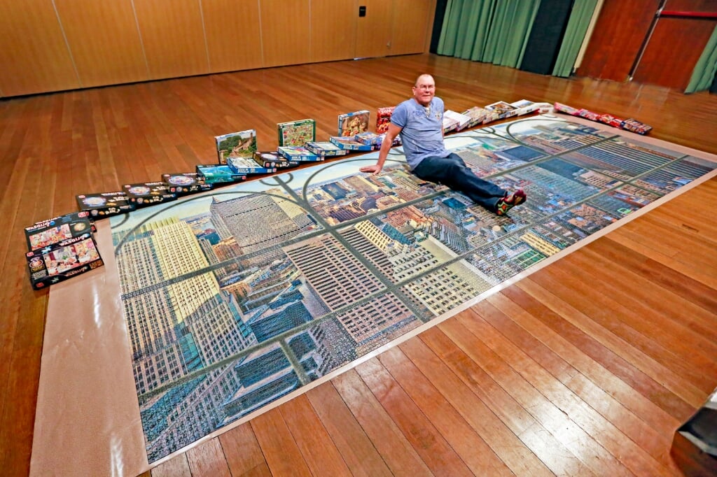 Cees poseert op zijn puzzel van 24.000 stukjes. De puzzels eromheen zijn te leen.