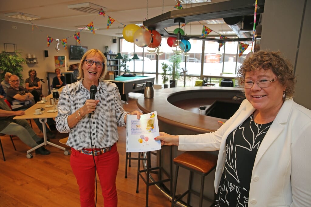 Carolien overhandigt het eerste exemplaar van het jubileumboekje van Activiteitendag de Horst aan wethouder Annette Groot van gemeente Heerhugowaard.