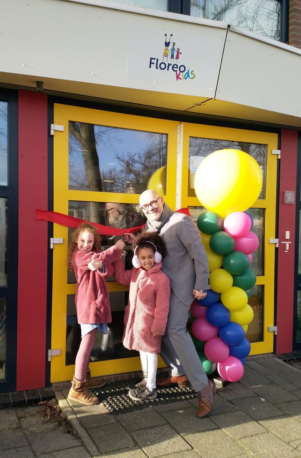 Hyabel, Sara en Johan Vriesema knippen het lint  door bij Kindcentrum Woubrugge.
