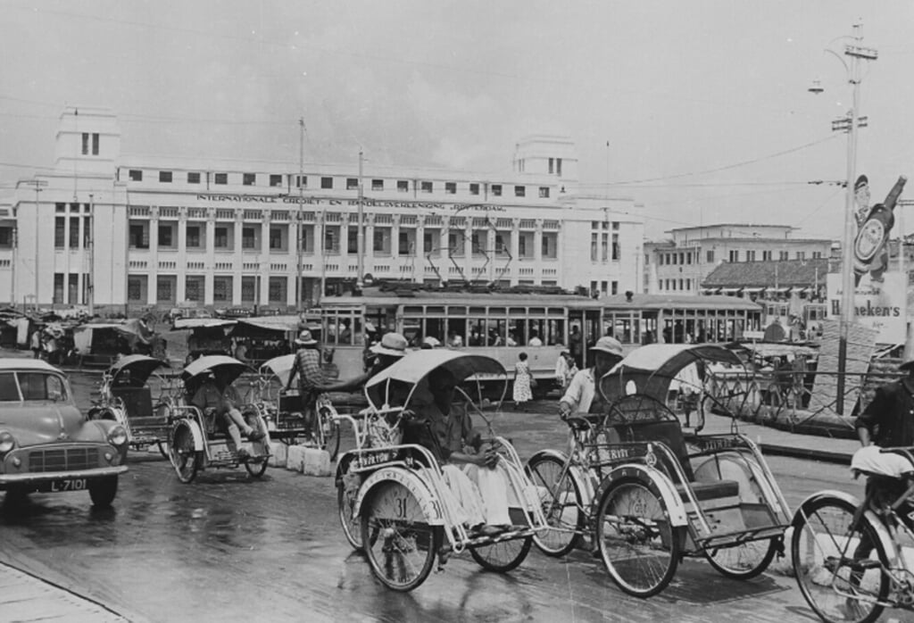 Fietstaxi's, auto's en een tram op het kruispunt voor het kantoor tussen 1953 en 1960