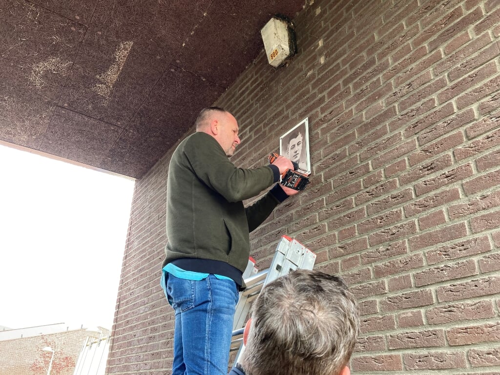 De foto wordt onder toezicht van Johan Kox in het poortje opgehangen. 