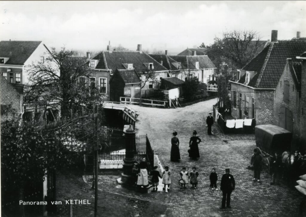 Het centrum van het dorp Kethel omstreeks 1905, gezien vanuit een woning op de hoek van de Dorpsstraat, Noordeinde en Schiedamseweg, in de richting van de Kerklaan, de weg naar links bij het witte hek. Op de voorgrond staan kinderen bij de 'Verspeekpomp'. Rechts de paardenstal van de Vergulde Valk. 