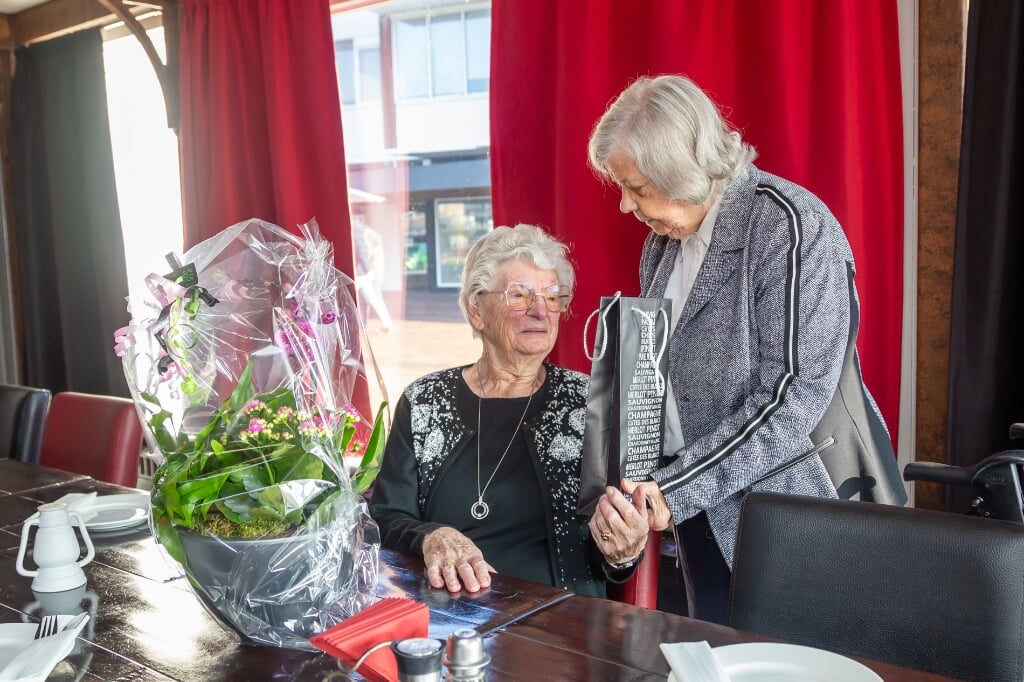 Ria de Sutter overhandigt de 103-jarige Rens Wolfert een fles rum, nadat de bloemen van de dorpsraad al op tafel zijn gezet. 