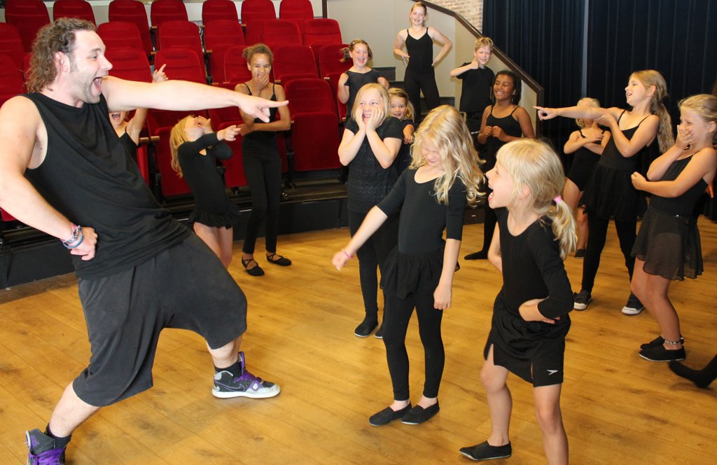 Docent Menno Leemhuis (links) laat kinderen enthousiast kennismaken met de wereld van zang, dans en toneel.