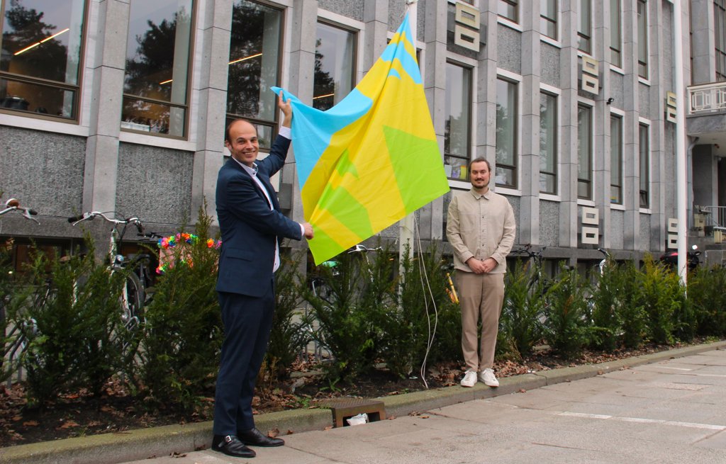 Wethouder Gijs van Malsen en Iskander Abspoel, consulent Discriminatiebestrijding hijsen de mensenrechtenvlag voor het Huis van de Stad.