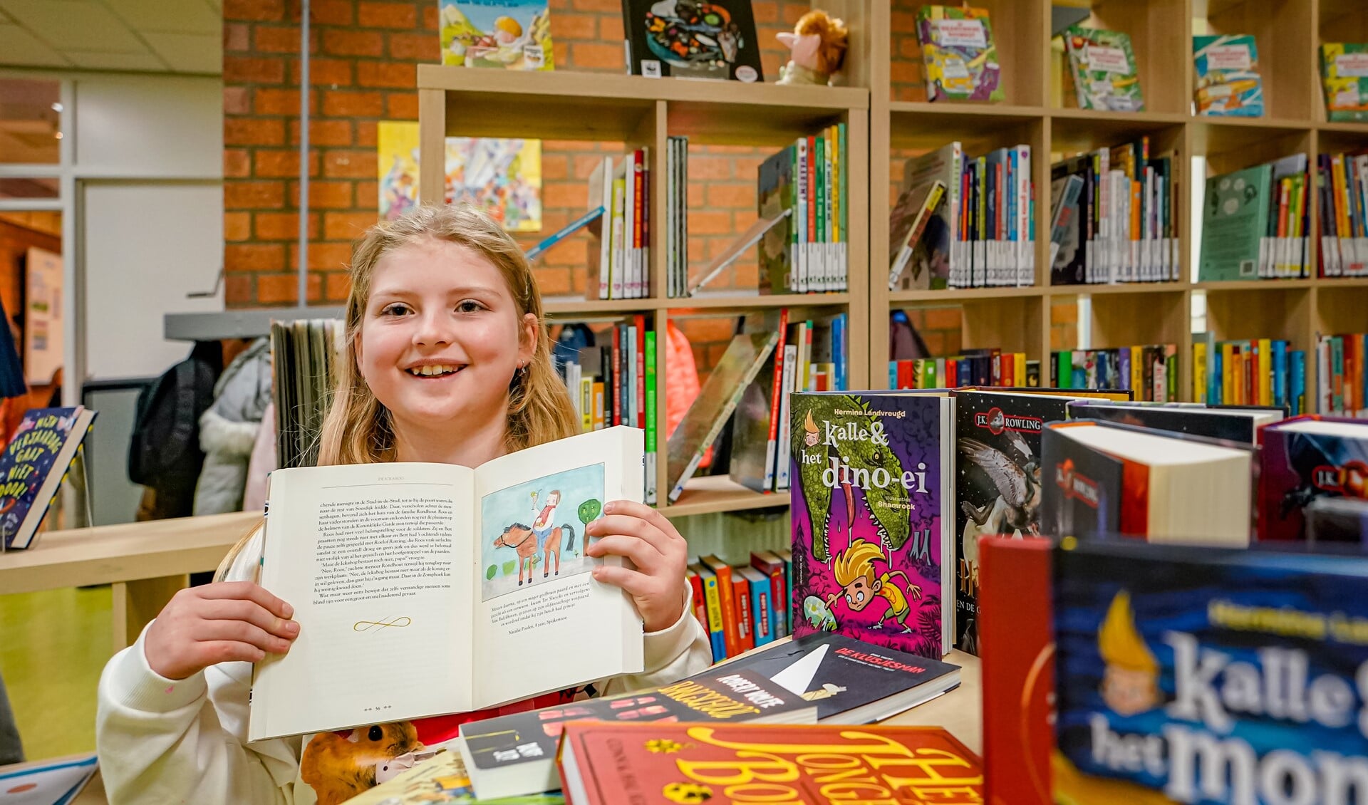 Natalie Poolen laat, in de nieuwe schoolbibliotheek, trots haar tekening in het boek van J.K. Rowling zien. 