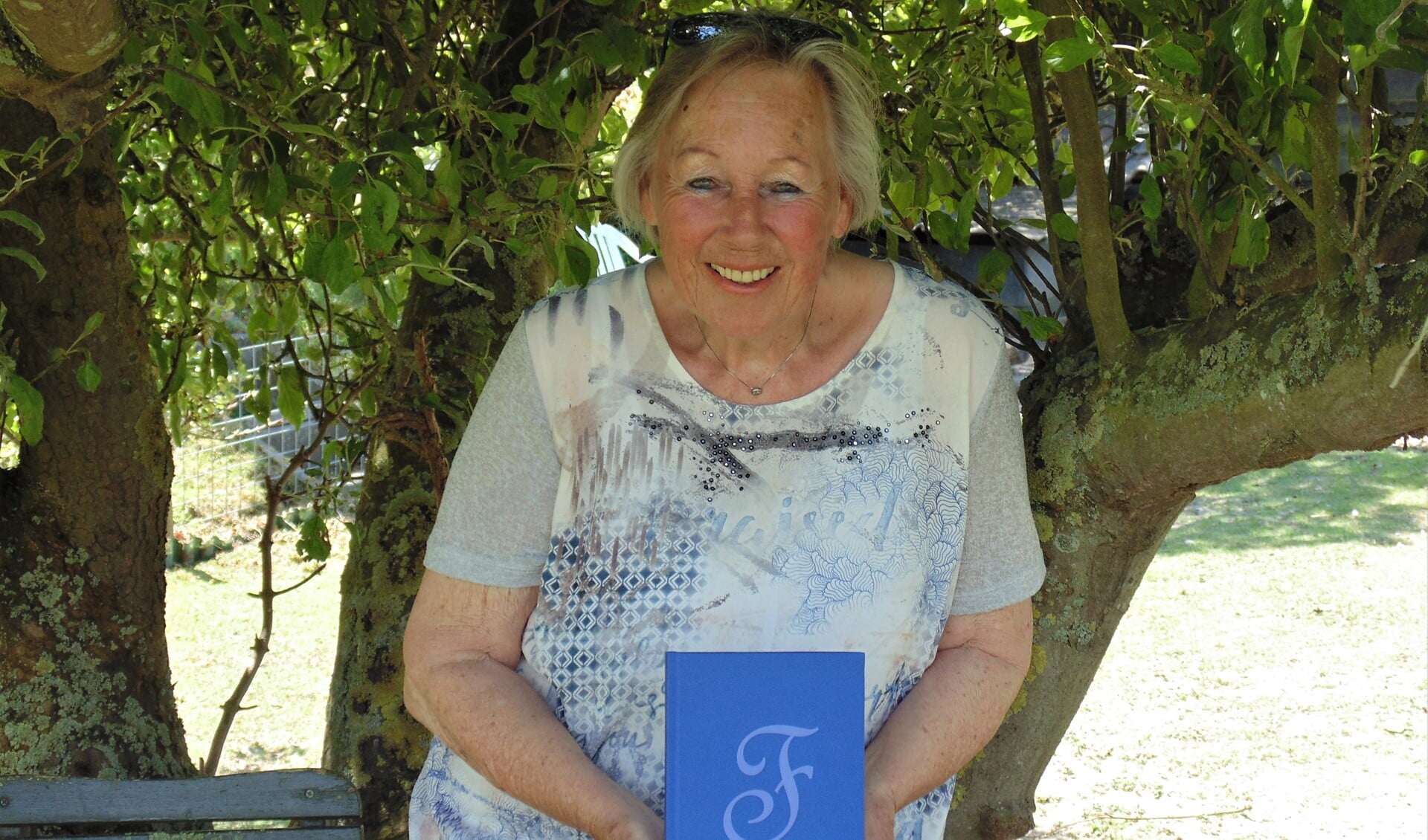 Frouke Bienefelt met haar gedichtenbundel in haar tuin. (Foto: Cora de Boed)