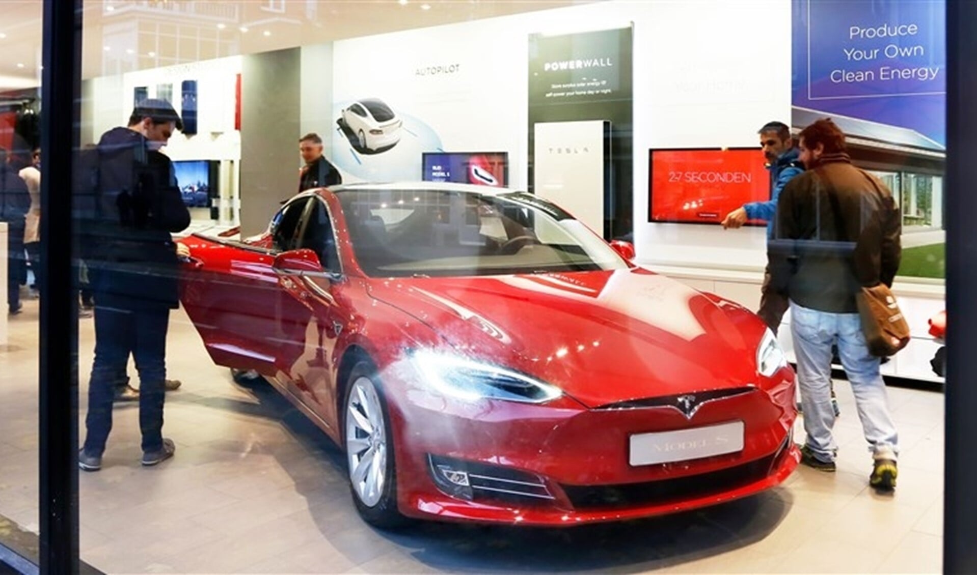 Geinteresseerden bekijken rode Tesla in winkel