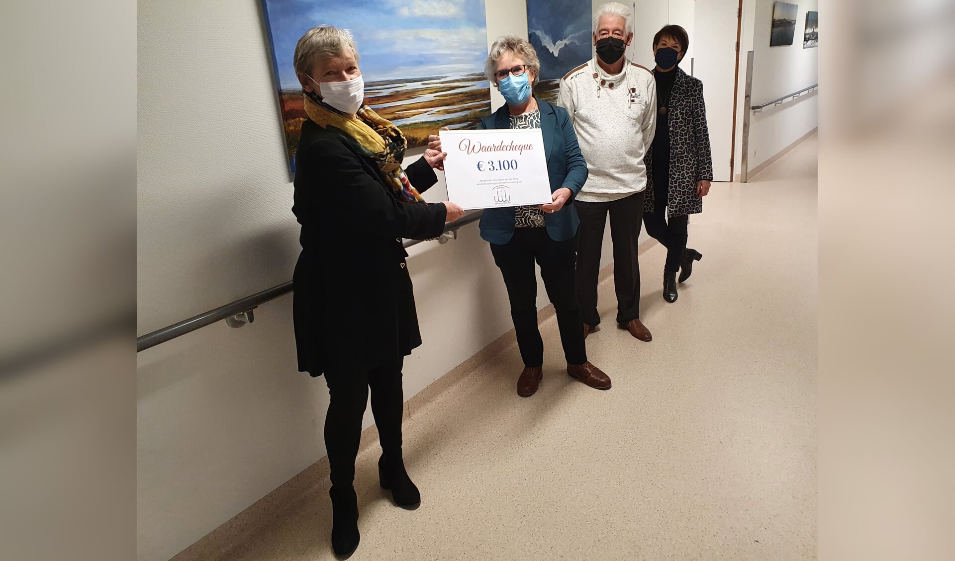 Kunstenares Jeanet van der Kamp (re) overhandigt de cheque aan penningmeester van de stichting Arna de Wit (li) in bijzijn van bestuursleden Karel Olsthoorn en Toos Buijs. 