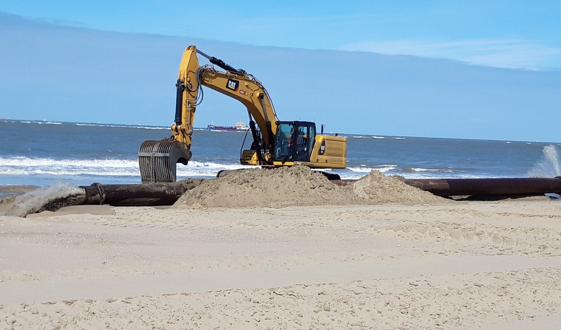 De sleephopperzuiger spuit het zand door de persleiding op het strand. De graafmachine zorgt voor de gelijkmatige verdeling.