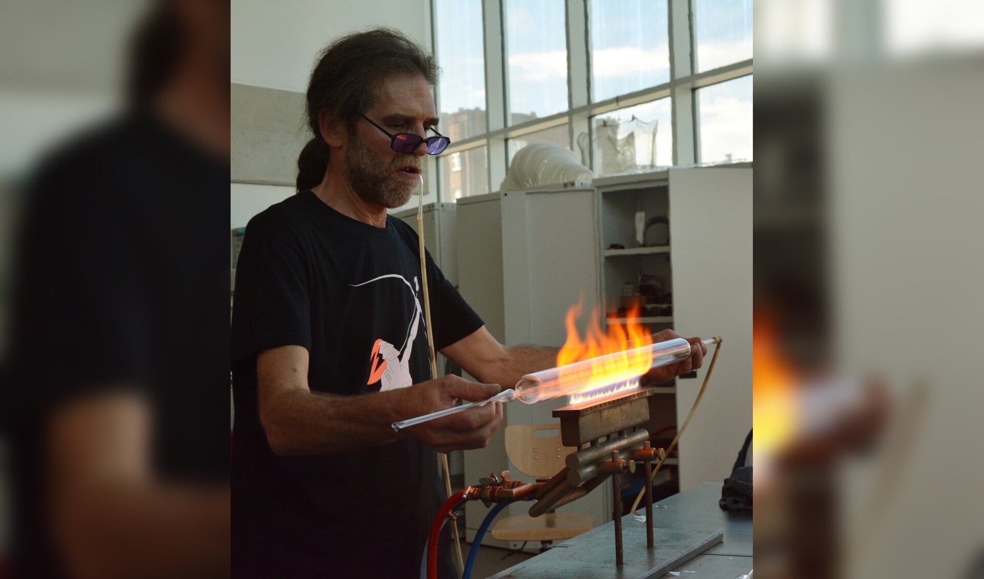 Duitse glasmeester Jörg Hanowski aan het werk aan de brander. N.B. let op de slang in zijn mond waarmee hij mini- glasblaast