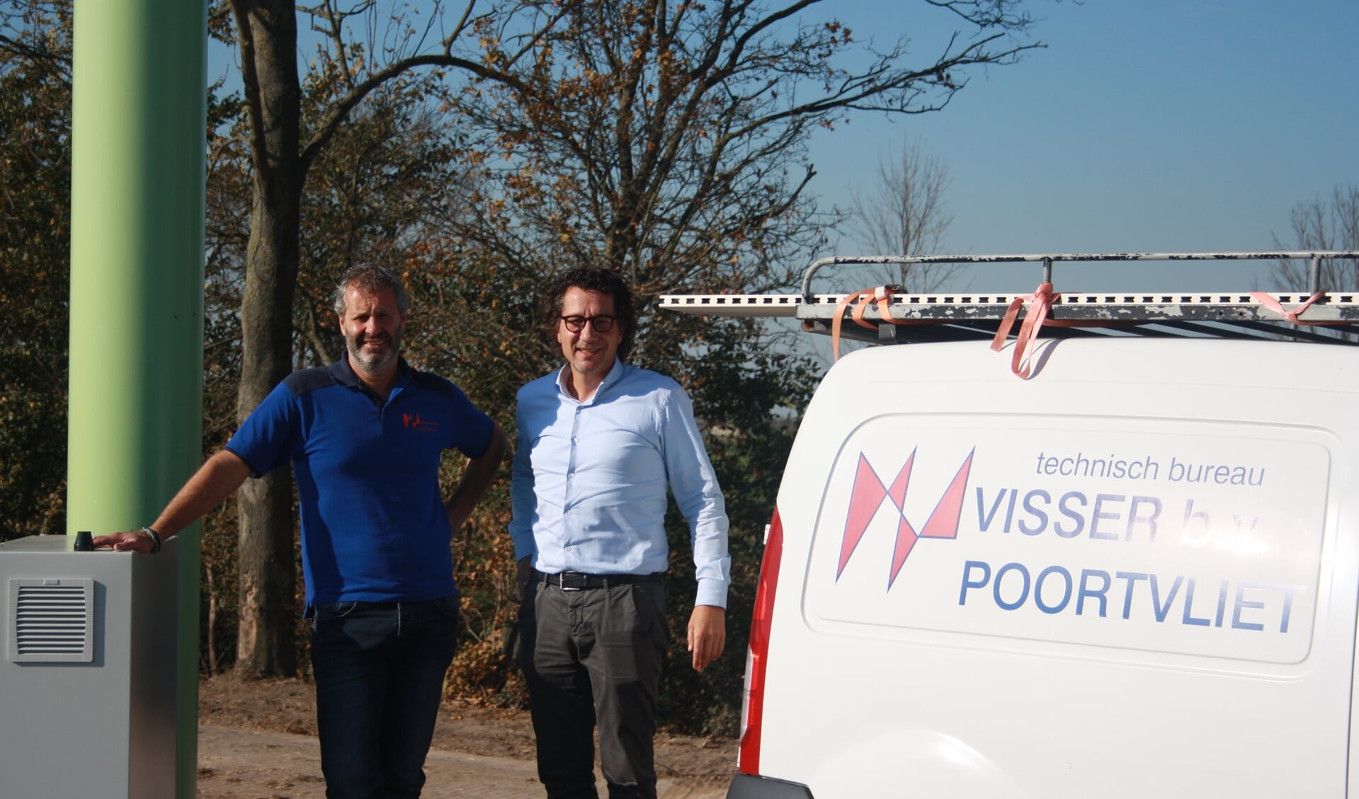 Links André Visser en rechts Ad Duvekot bij één van de bedrijfsauto's onder een door het bedrijf geplaatste landbouwkundige windmolen.