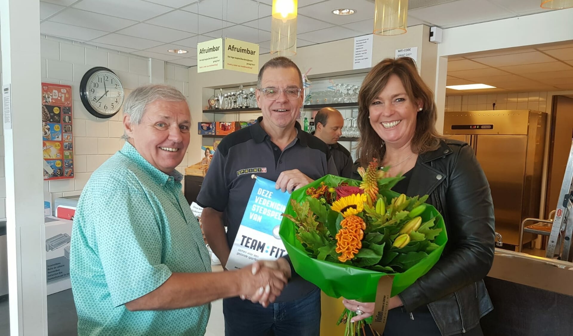 Henk van den Biggelaar (midden) en accommodatiemanager Johan de Koning (links) krijgen het zilveren vaantje uitgereikt van Karin Potting 