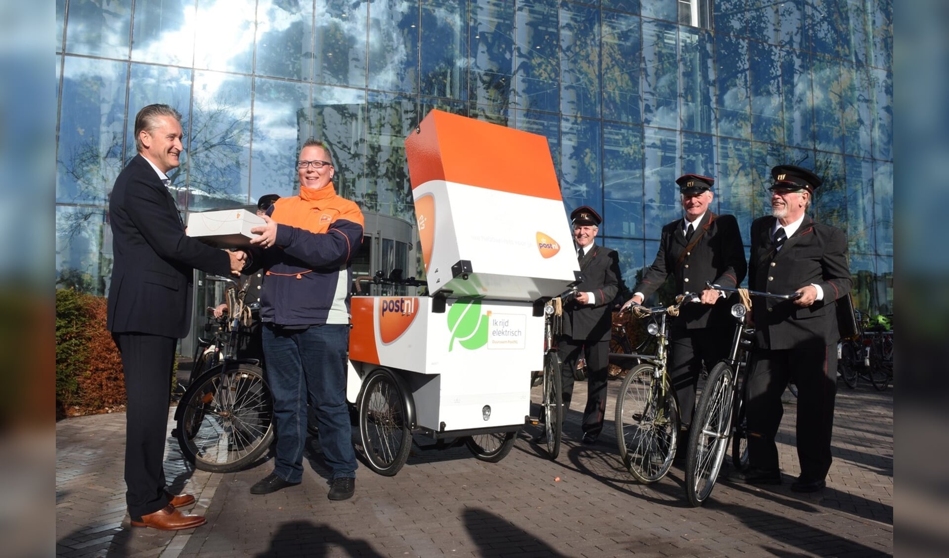 Jack Doomernik neemt het duurzame pakketje in ontvangst in het bijzijn van de ouderwetse postbezorgers 