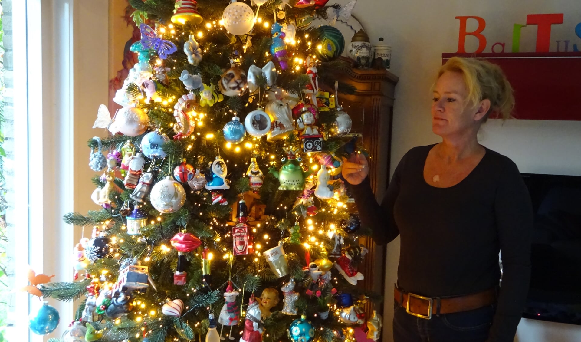 Monique Baltus bij haar kerstboom vol ornamenten met een verhaal.