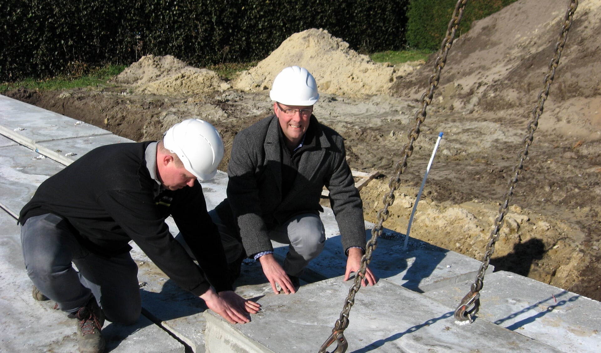 Wethouder René Lazeroms (rechts) legt een van de vloerplaten voor de nieuwe NOM woningen in de juiste positie.
