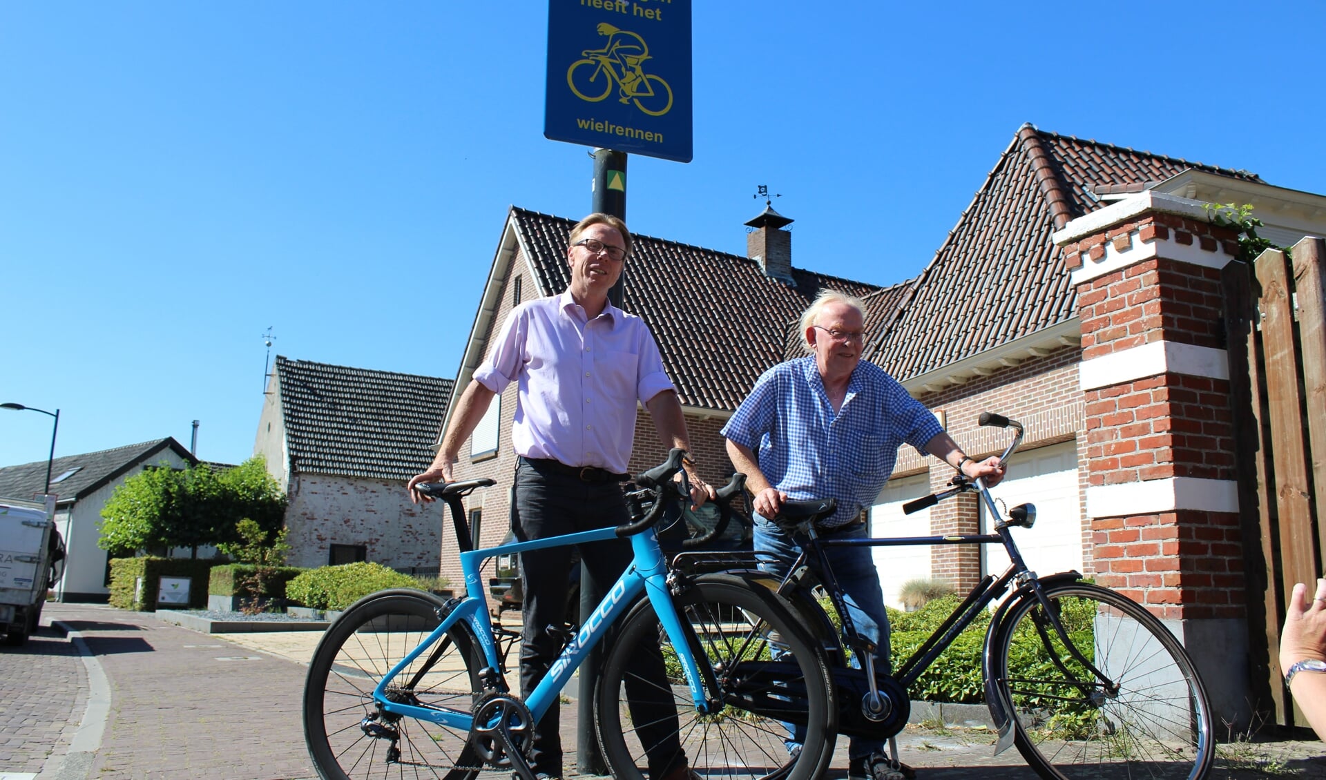 Lars van der Beek en Wil de Jong poseren bij het bord 'Huijbergen heeft het Wielrennen'