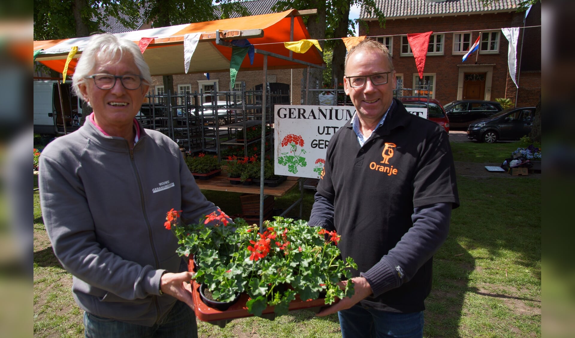 Marktmeester Jos Verdonk van de geraniumcommissie overhandigt symbolisch een aantal geraniums aan Peter van Oosterbosch van Harmonie en Malletkorps Oranje, die volgend jaar de organisatie overnemen. 