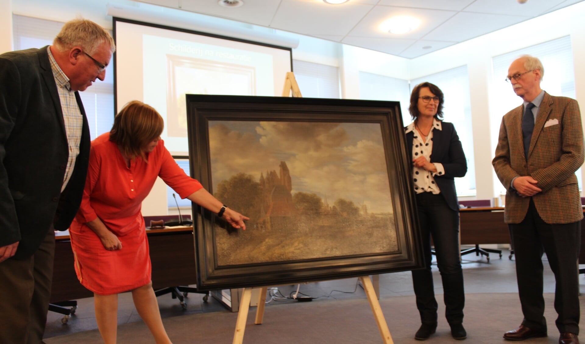 Wethouder Baartsmans wijst naar de mensen op het schilderij die na restauratie weer zichtbaar zijn geworden.