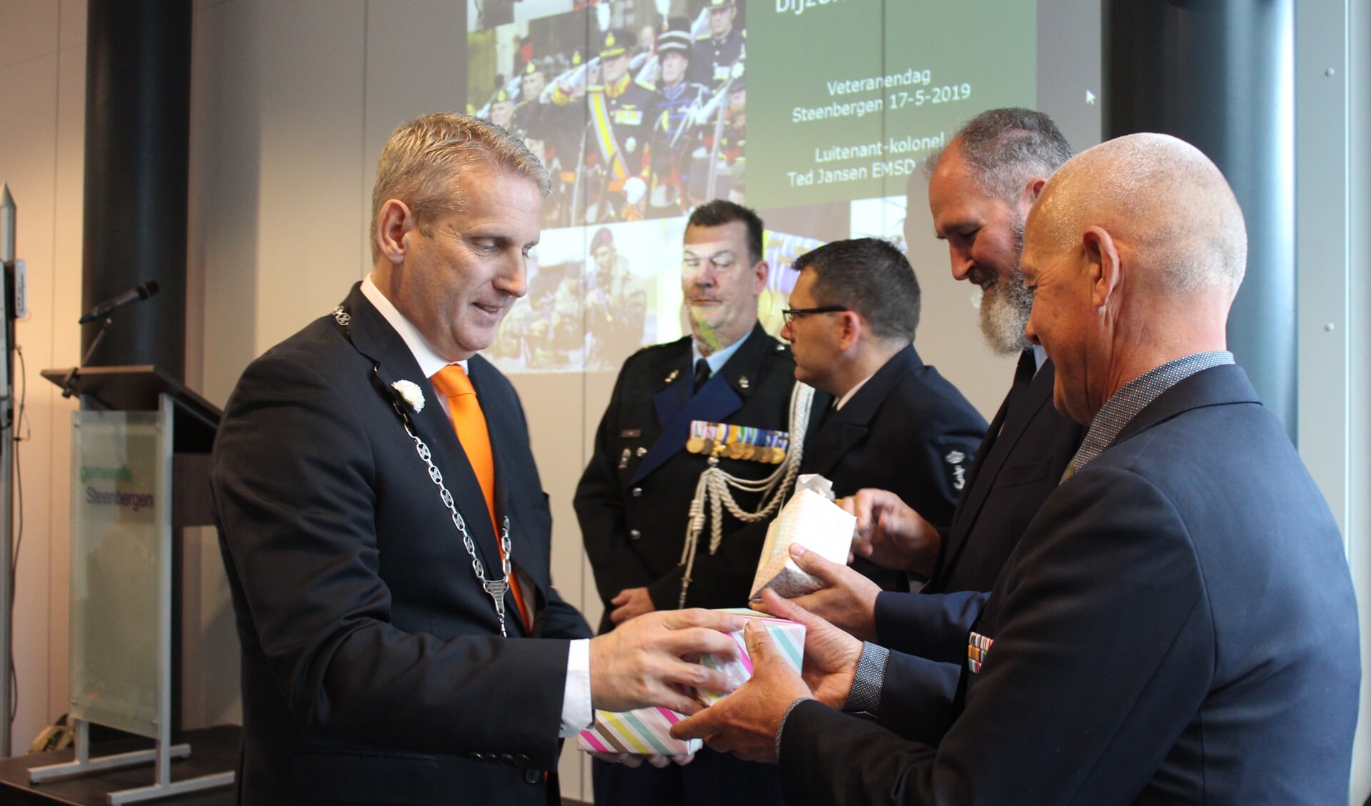 Burgemeester Van den Belt deelt een glasgeschenk uit aan bestuursleden van Veteranen Steenbergen (VEST)