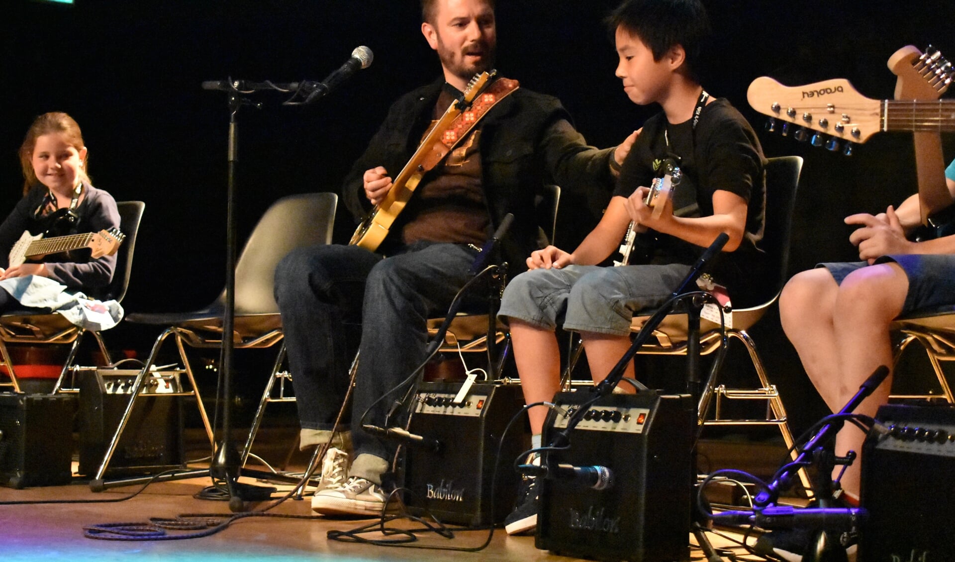 Peetman begeleidt jonge gitaristen op het podium.