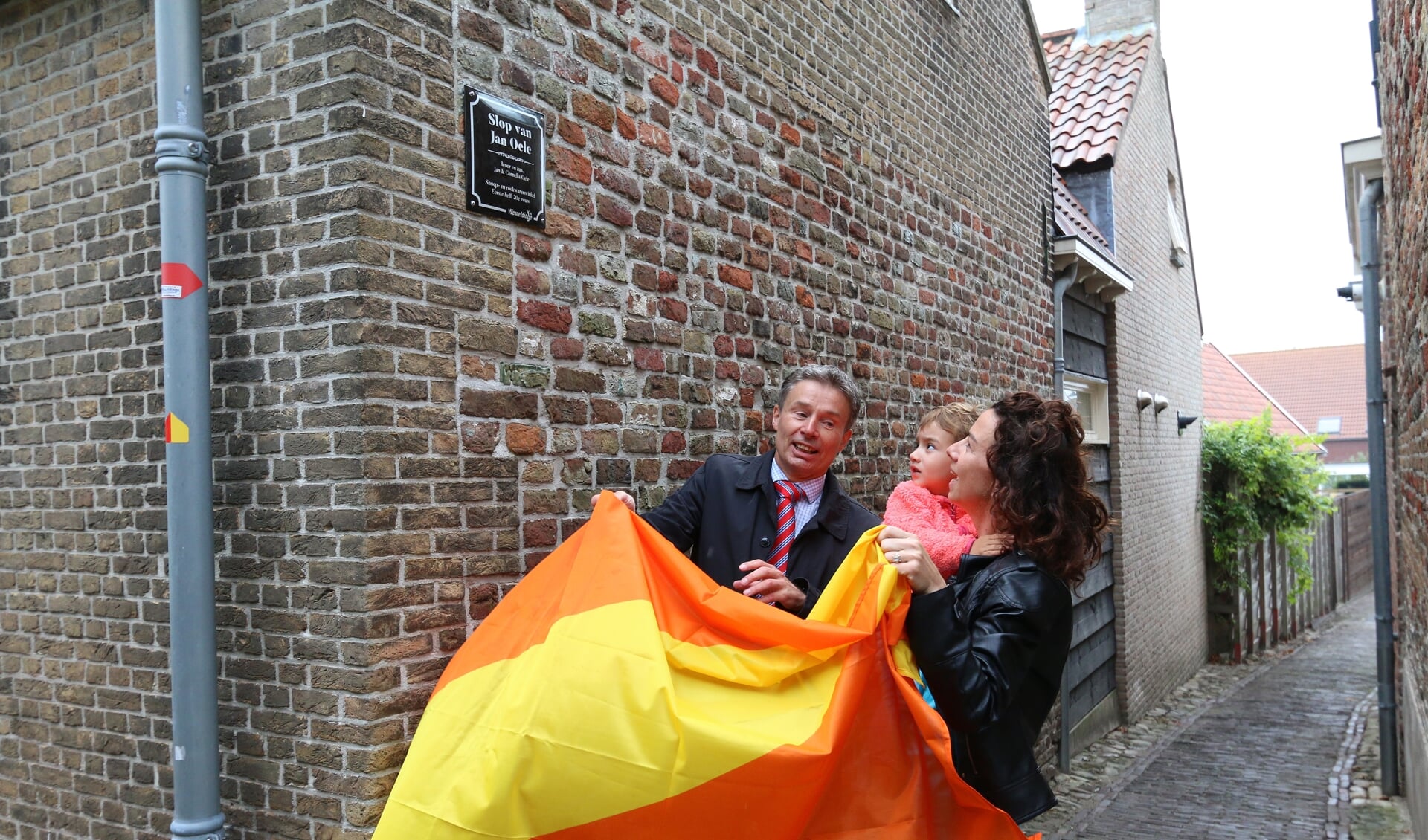 Willemien en Zoë Mallekote onthullen op de muur van hun huis, samen met burgemeester Huub Hieltjes het bordje van 'het slop van Jan Oele'.