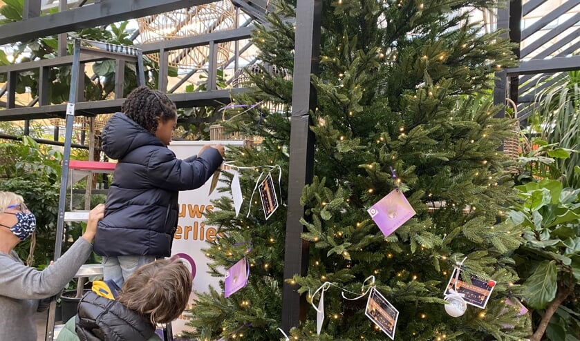 Kinderen hangen een wens in de kerstwensboom.