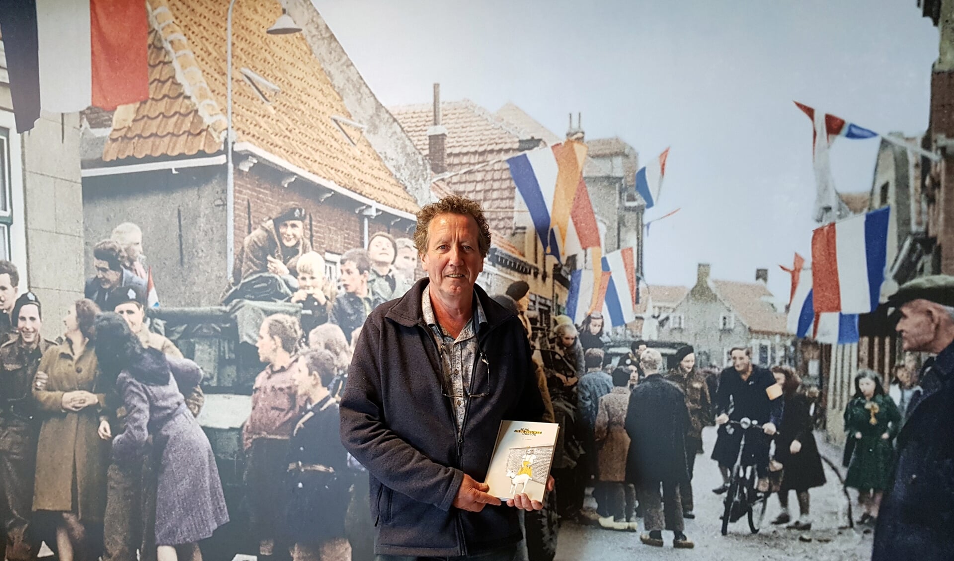 Jan van Damme, met zijn boek, voor één van de levensgrote foto's van de bevrijding in het Bevrijdingsmuseum Zeeland. FOTO EUGÈNE DE KOK 