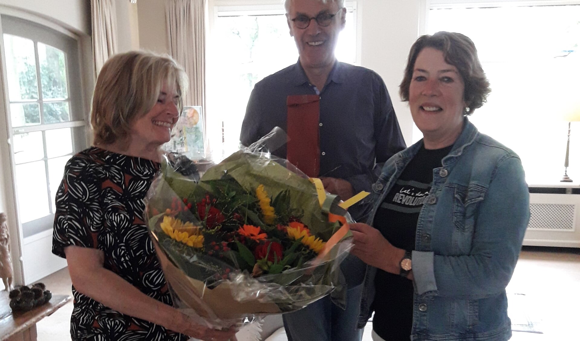 Voorzitter Maria van Nispen overhandigt de jubilaris een boekt bloemen. 