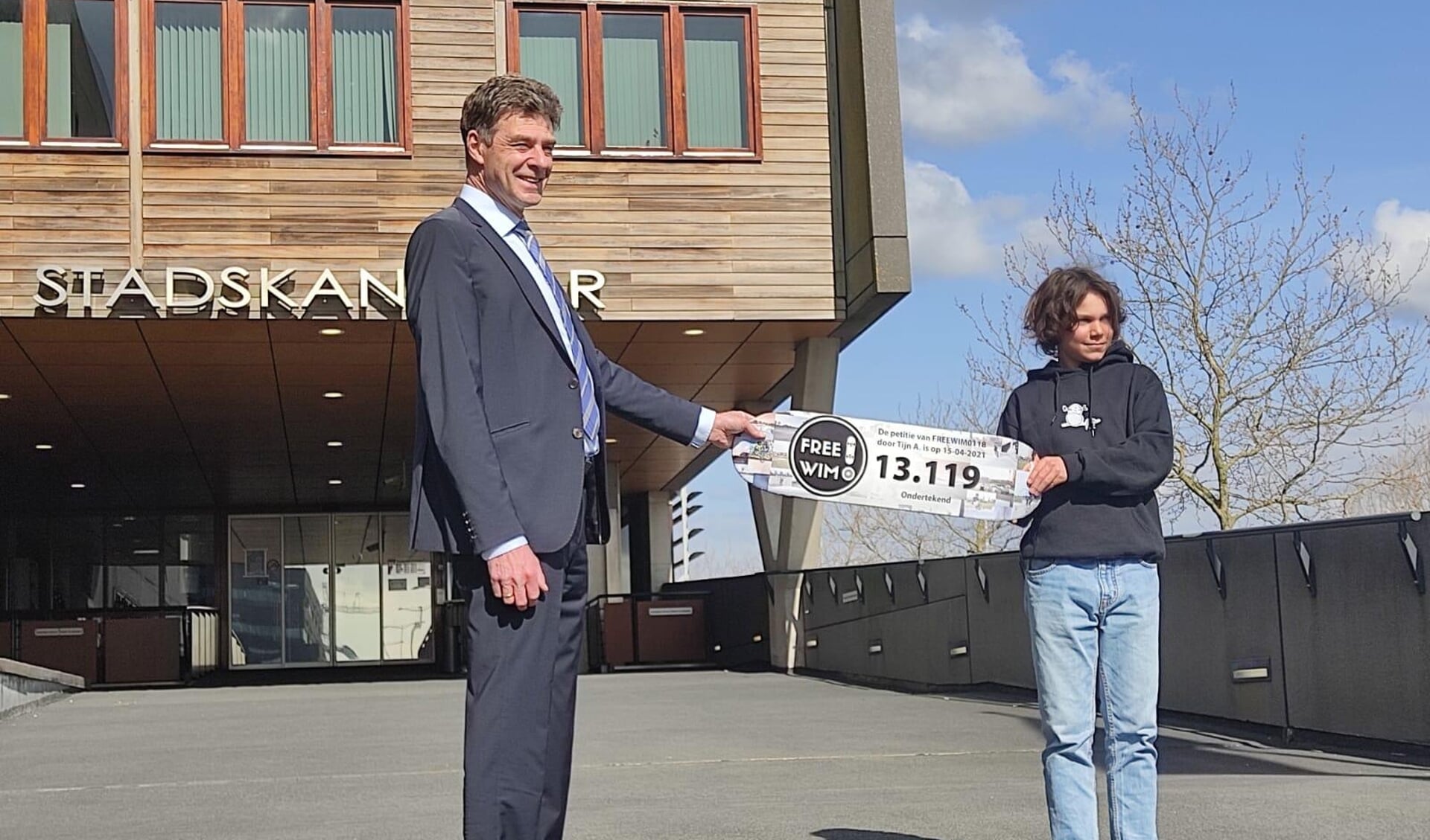 Tijn Anderson overhandigt het skateboard met handtekeningen aan wethouder Dekker