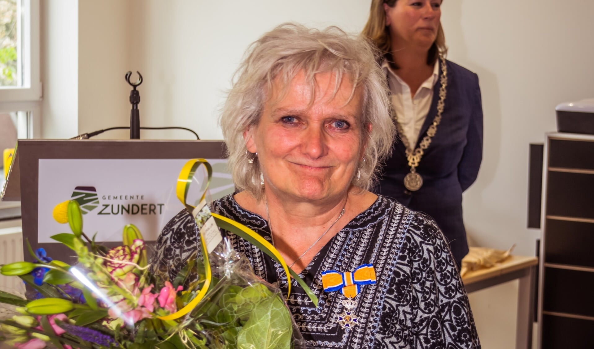 Marion van Bergen bij de uitreiking van haar Koninklijke onderscheiding. Op de achtergrond burgemeester Joyce Vermue.