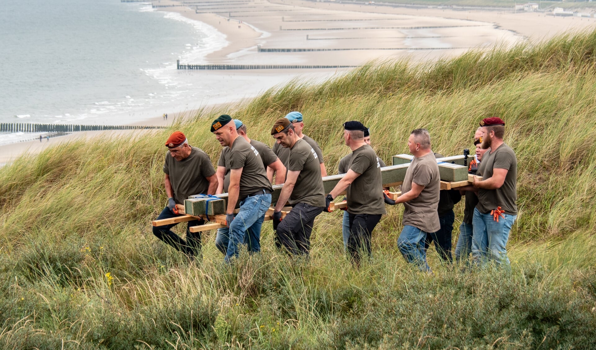 Veteranen dragen het nieuwe herdenkingskruis door de duinen van Valkenisse.