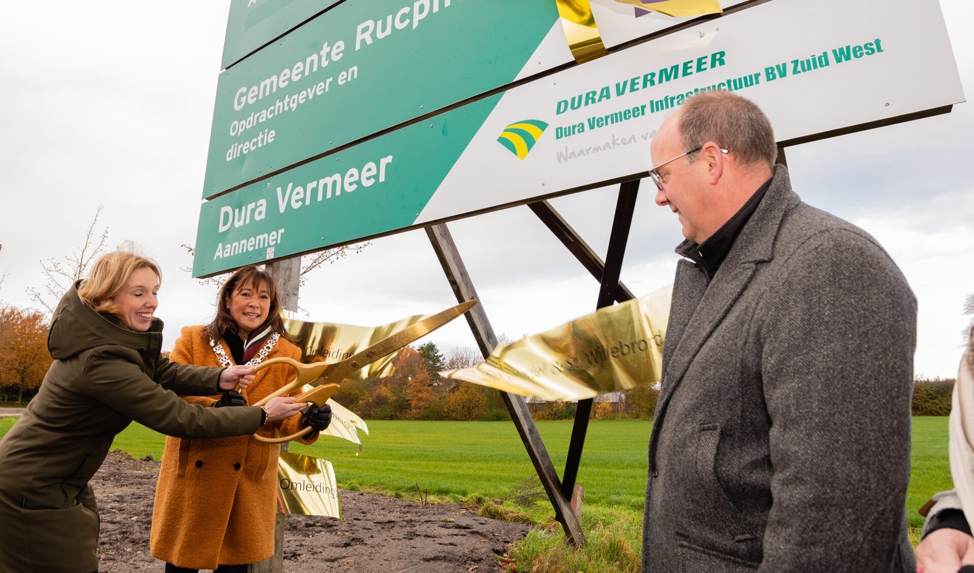 Bij de ovale rotonde wordt de afronding officieel met het doorknippen van een gouden lint door gedeputeerde Otters-Bruijnen (l) en burgemeester Van der Meer Mohr. Wethouder Lazeroms (r) kijkt toe. 