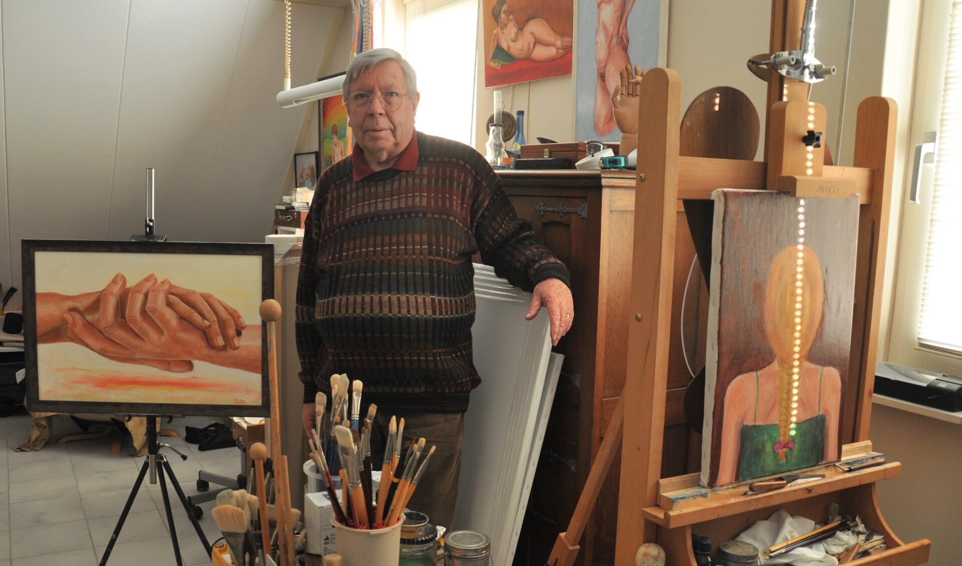 Henk Braet met zijn schilderij 'De Handen Ineen' in zijn atelier.