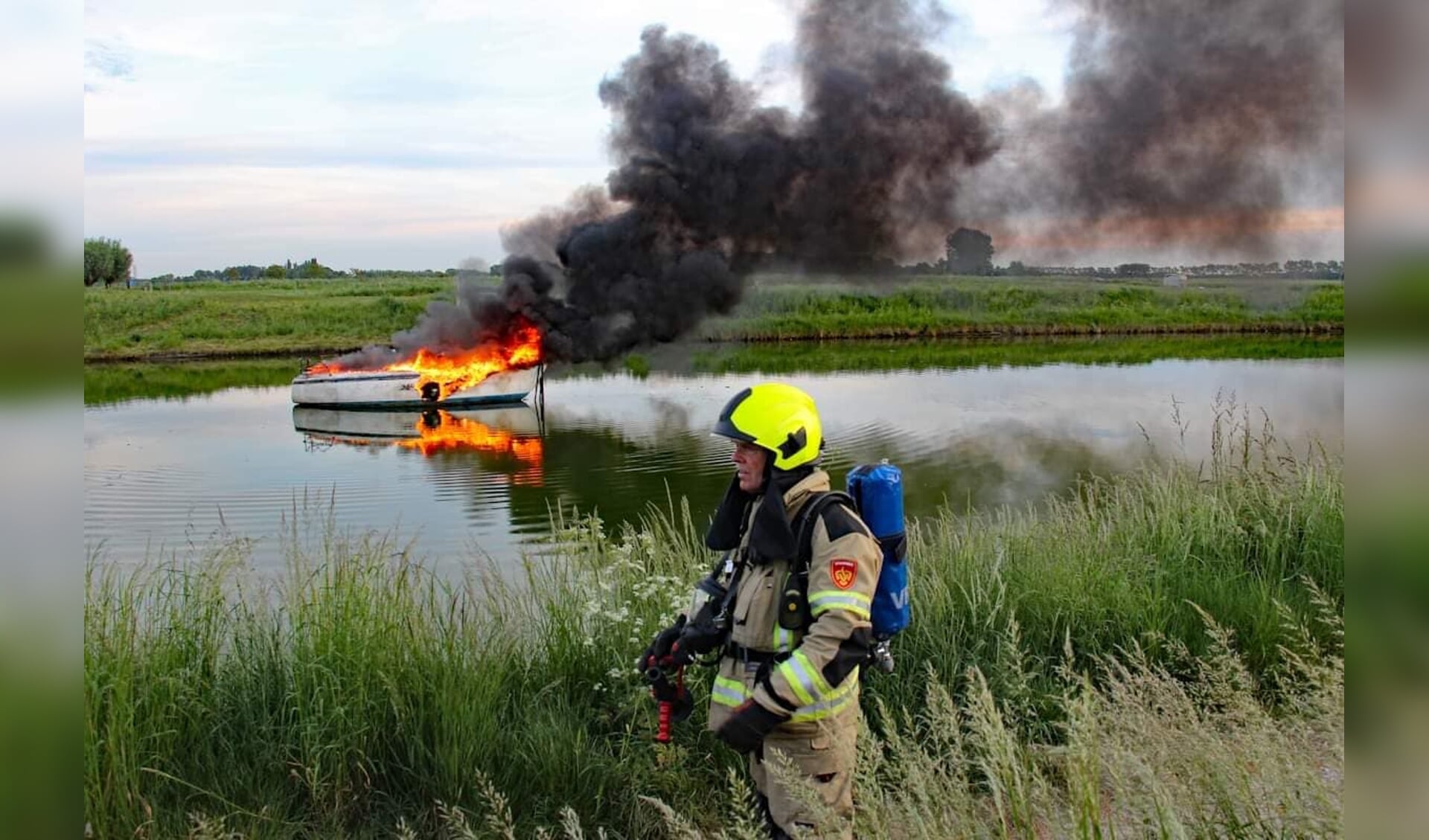 Een brandweerman staat voor het brandende jacht bij Arnemuiden