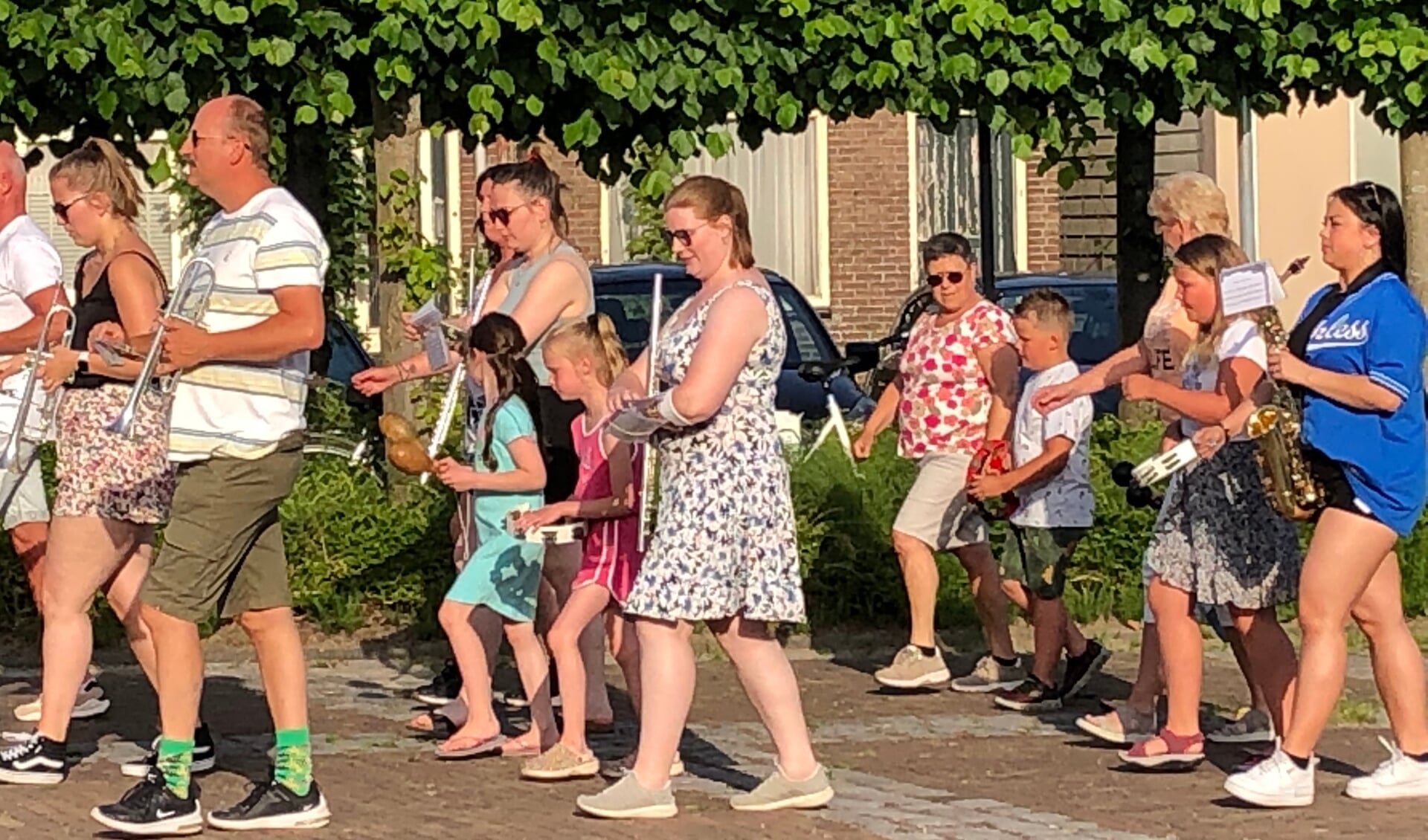 Een aantal kinderen loopt mee tussen de muzikanten tijdens een optreden in Biezelinge.