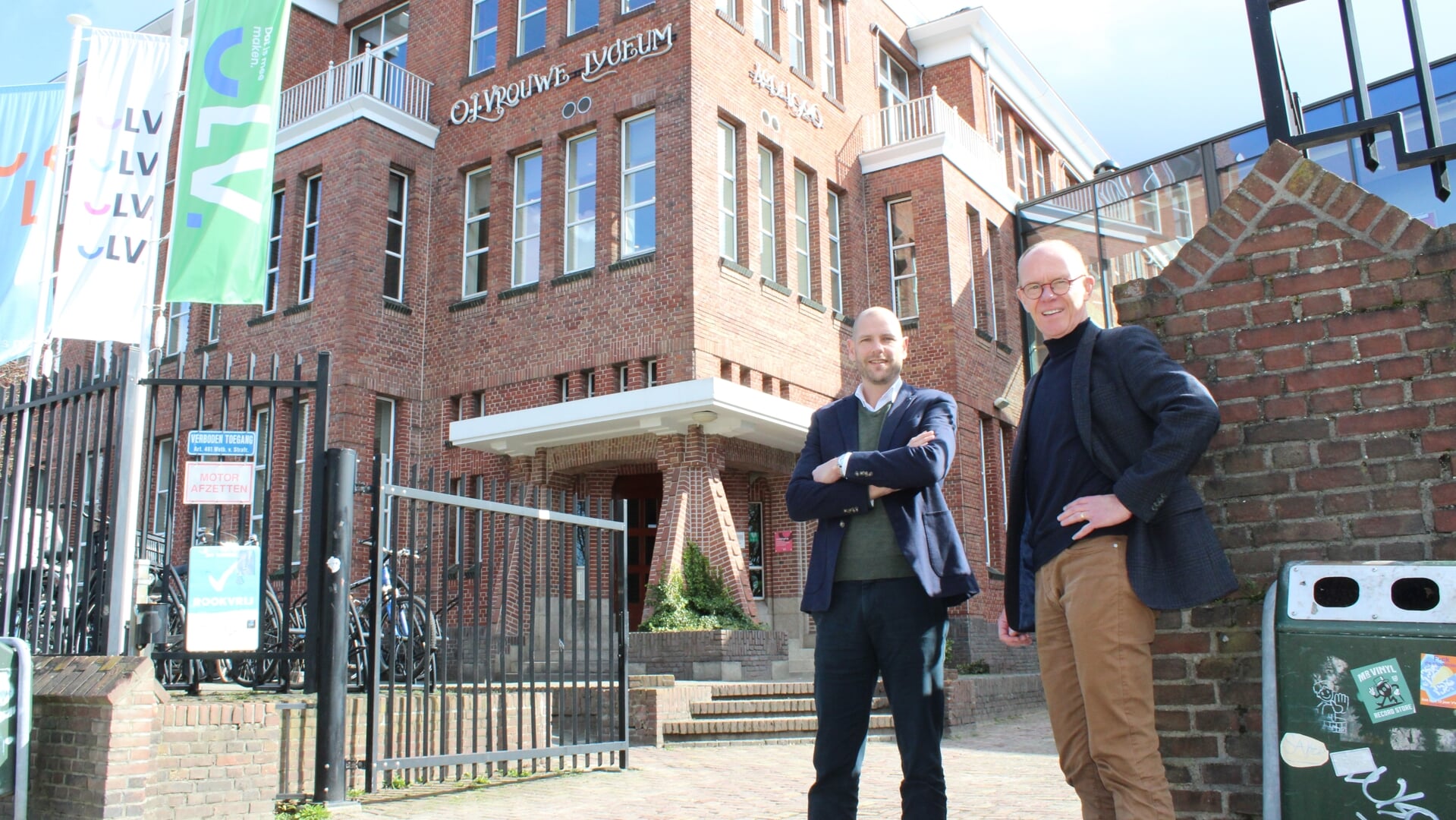 Tol Swinkels en Frits van der Zalm voor het OLV, met daarbij ook de vlaggen met het nieuwe logo van de school