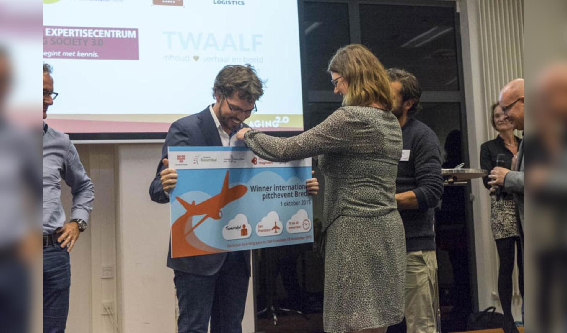 Pitchwinnaar Sjoerd Wennekes krijgt van wethouder Miriam Haagh een ticket overhandigd naar de Aging 2.0 pitchfinale in San Francisco.